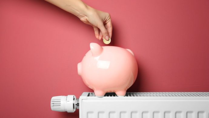 A coin being dropped into a pink piggy bank, sat atop a radiator
