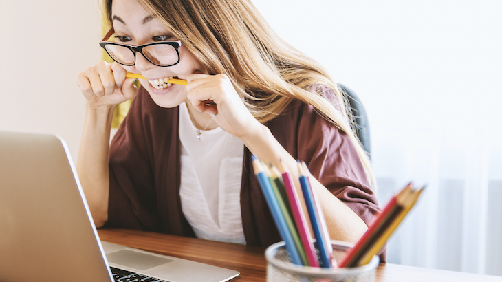 A woman sat at her laptop biting a pencil in frustration